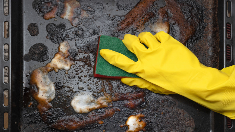 A person wearing yellow rubber gloves and scrubbing a burnt baking sheet.