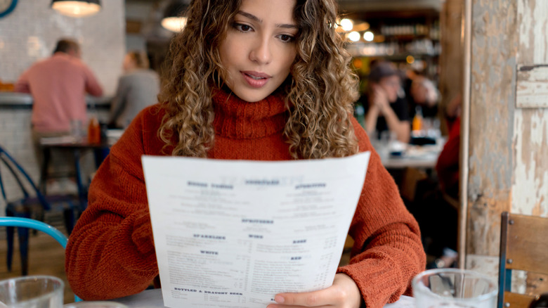 A woman wearing an orange sweater reads a restaurant menu
