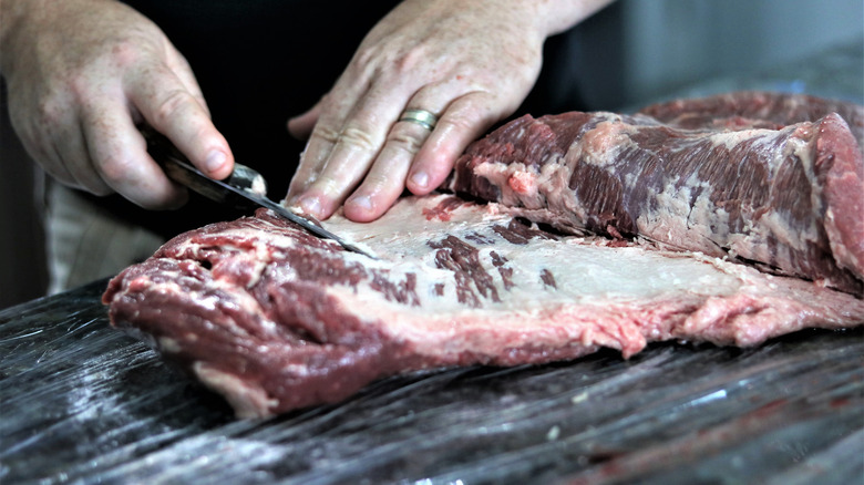 hands trimming fat from beef brisket