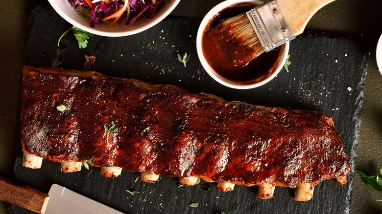 A rack of ribs on a platter with barbecue sauce and a brush
