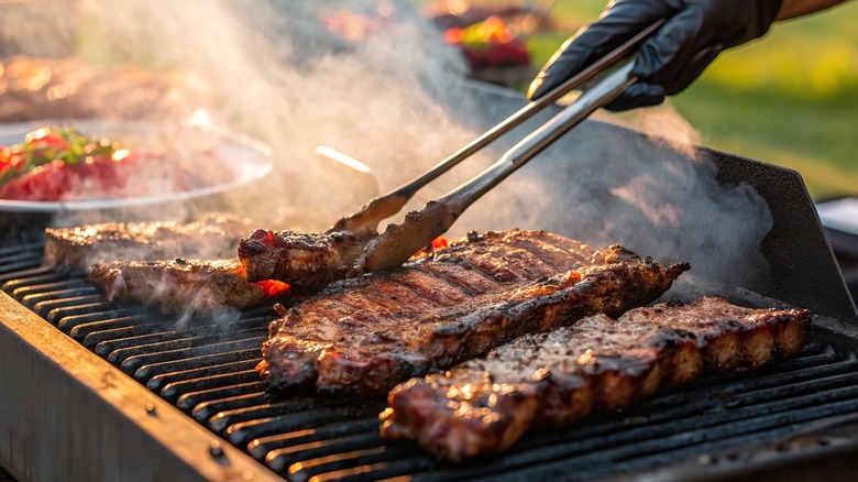 Person barbecuing meat over smoky grill