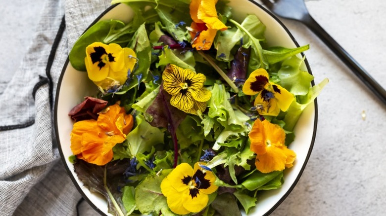 A bowl of salad with edible flowers including pansies and nasturtiums.
