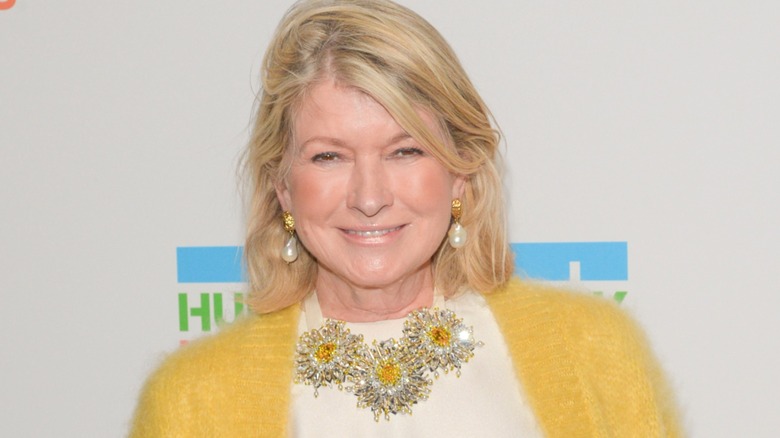 Martha Stewart smiling for the camera dressed in a silk shirt and yellow sweater.