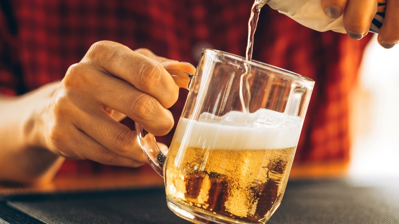 Hand pouring beer into glass mug