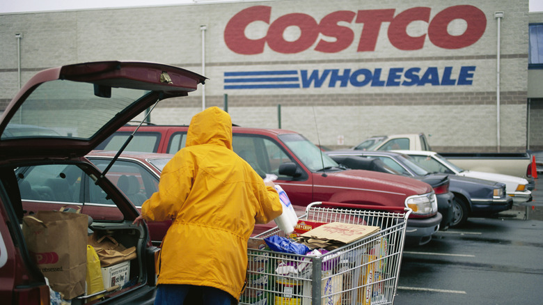 Customer in raincoat puts groceries in car outside Costco