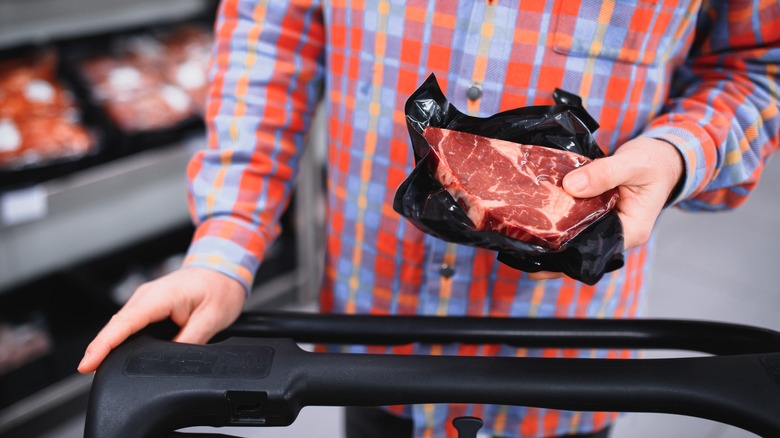 Man holds packaged raw steak at grocery store