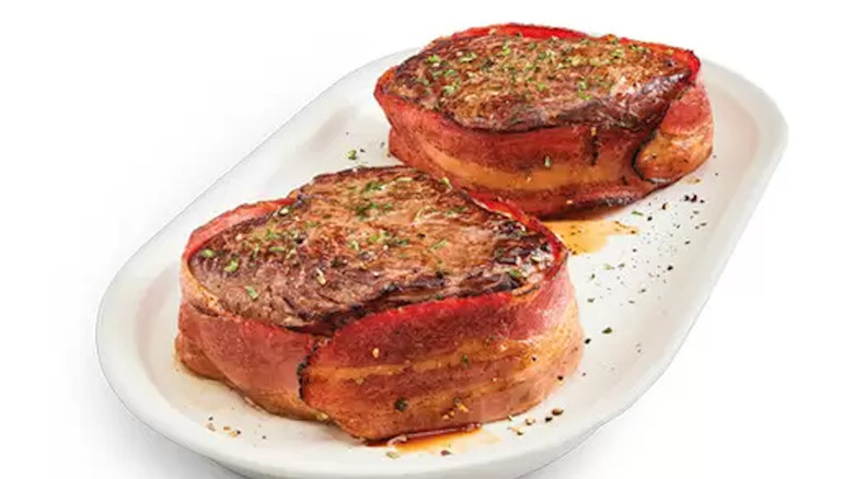 two bacon wrapped filets with seasoning on white plate