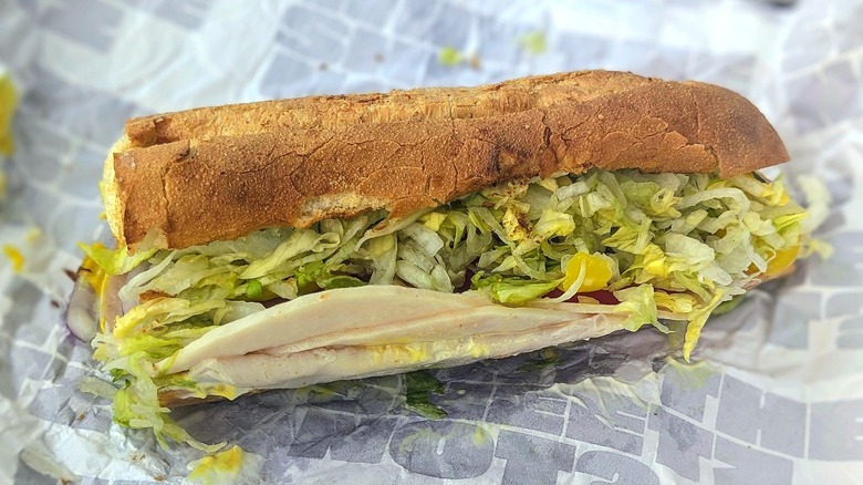 A messy 6-inch turkey sub with lettuce and mustard on white paper