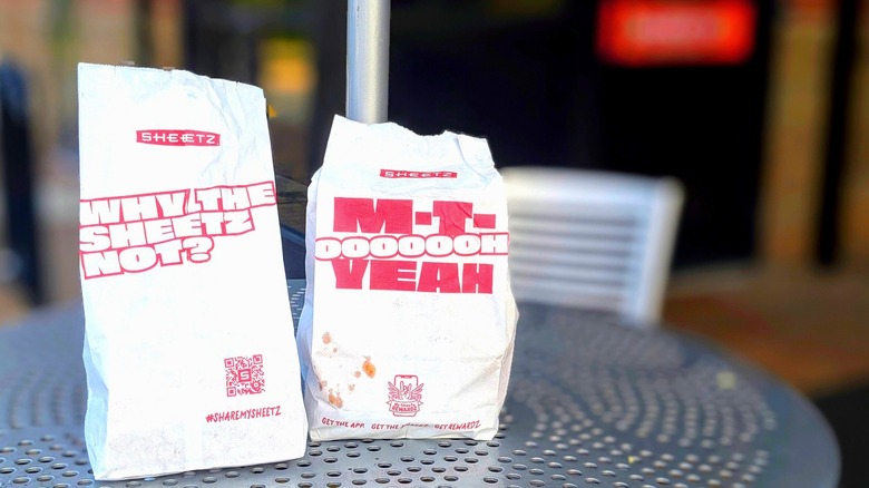 Two greasy white paper Sheetz bags on a metal picnic table in front of the store