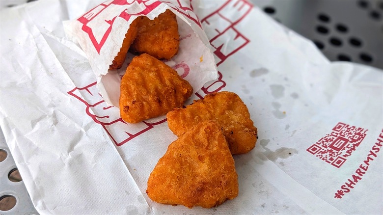 Fried, breaded macaroni and cheese bites spilling out of a bag on white Sheetz-branded paper