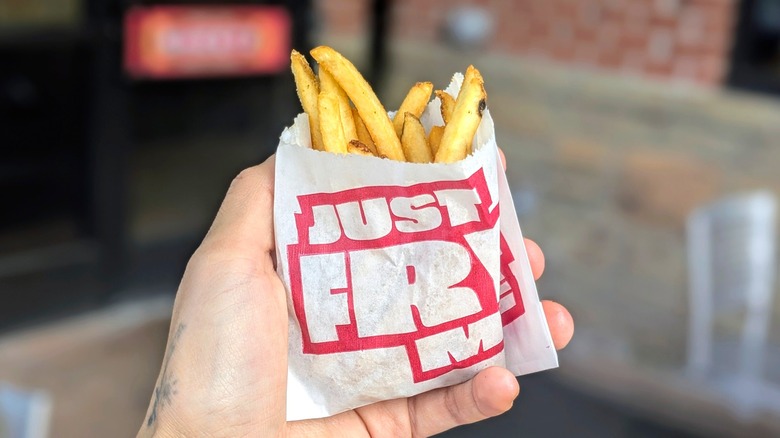 A hand holds a small paper bag of french fries with the Sheetz entrance in the background