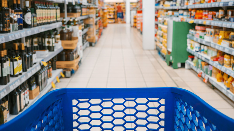 Shopper's perspective of a grocery cart moving down a liquor and supplement aisle