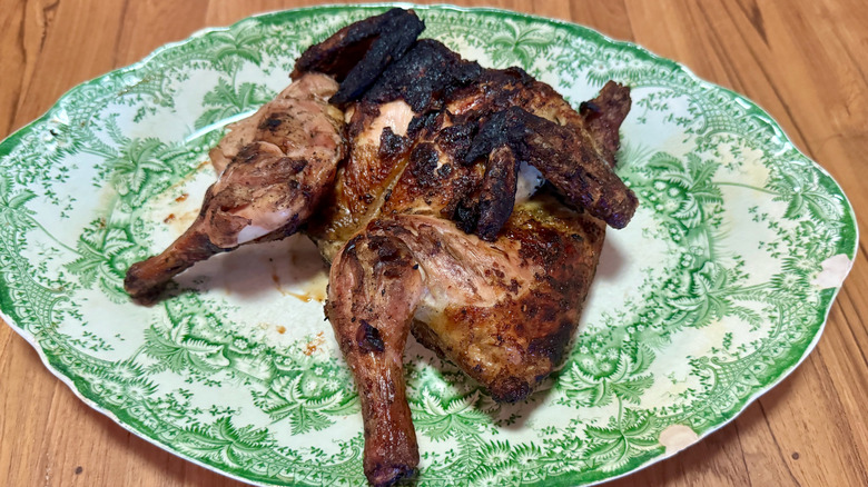 A grilled spatchcocked chicken on a green and white serving platter.