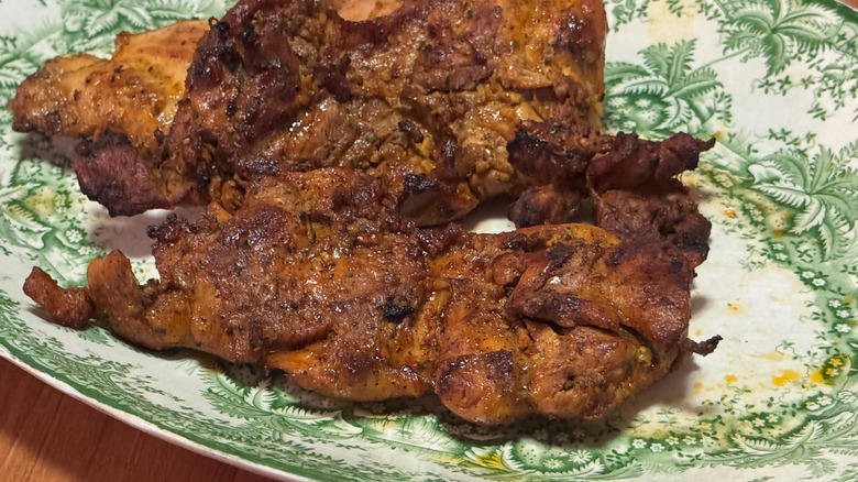 Plump, orange hued grilled chicken thighs on a green and white platter.