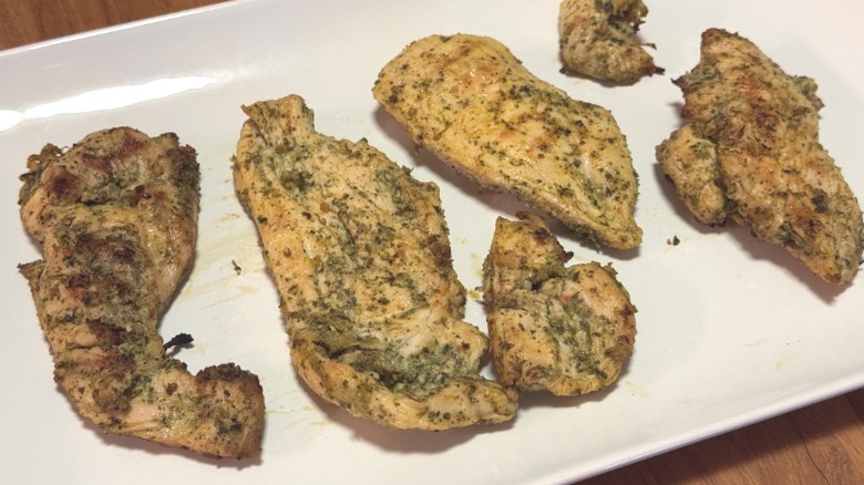 Six thin pieces of grilled chicken breast with a green pesto marinade on a large white serving platter.