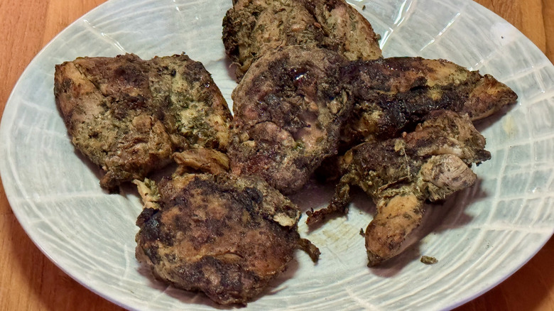 A pile of grilled boneless skinless chicken thighs on a white plate.
