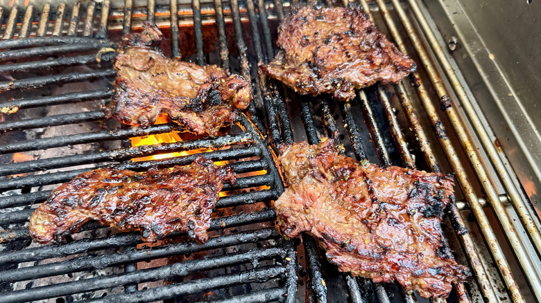 Four skirt steaks on a grill over open flames.