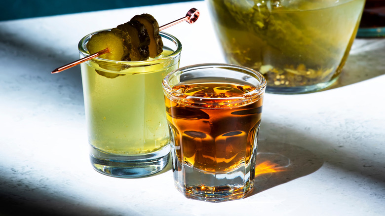 Shot glasses of whiskey and pickle juice with pickles become a pickleback shot