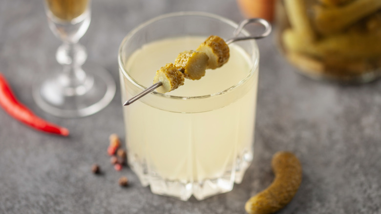 A cocktail of pickle brine and pickle garnish in a rocks glass