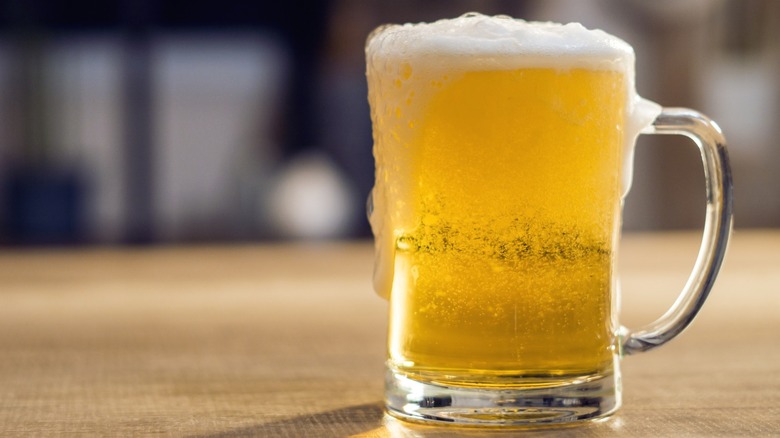 A mug of beer sitting on a wooden surface.