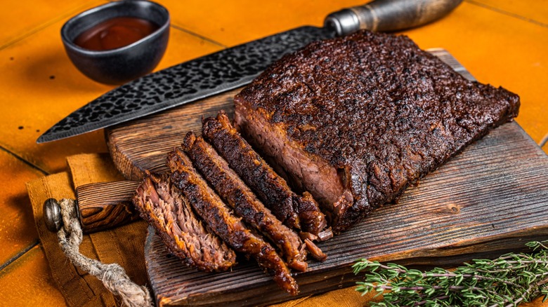 Smoked Barbecue Beef Brisket with Sauce on wooden board. Orange background. Top view.