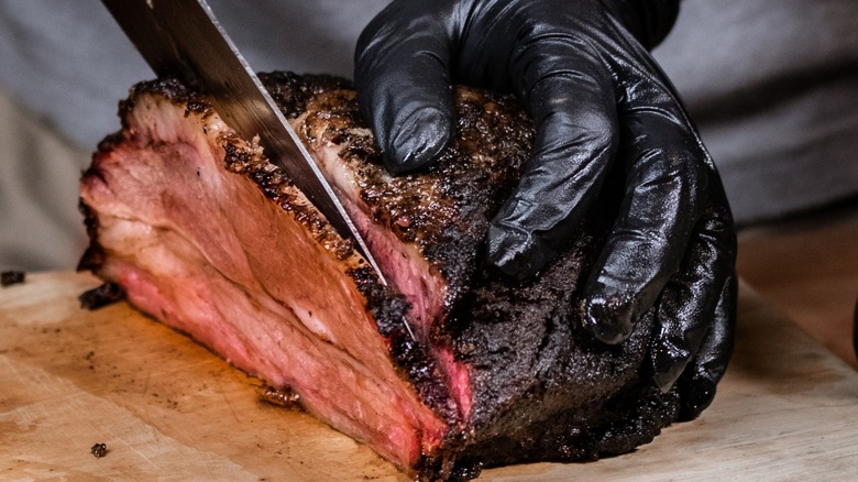 gloved hand holding a knife Slicing Smoked Beef Brisket