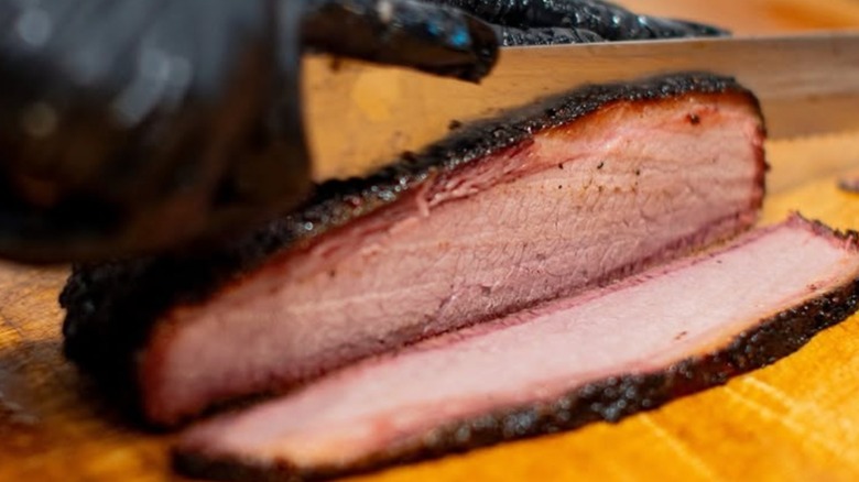 Gloved hand cutting slices of Brisket on wooden cutting board from Prime Barbecue
