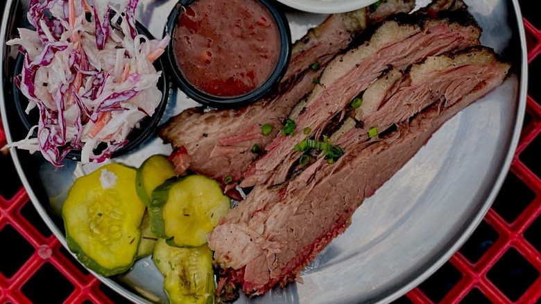 Sliced brisket with sides of slaw, sauce, and pickles from Great Northern BBQ Co