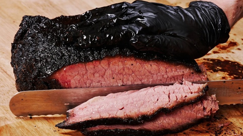 Gloved hand slicing brisket on wooden cutting board at Lewis Barbecue