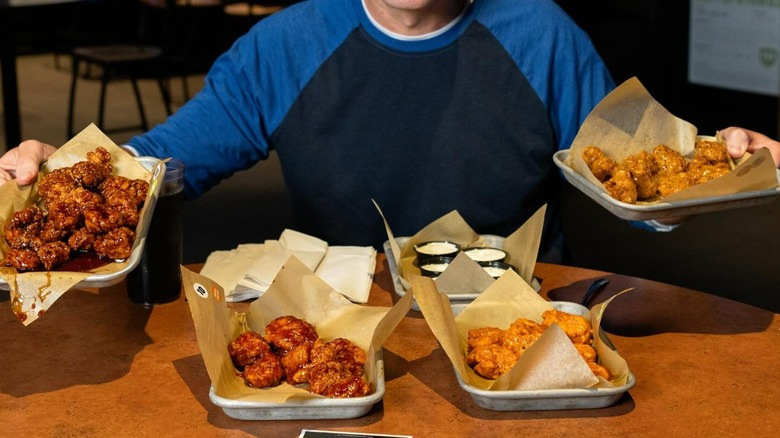 person holding two trays of boneless wings while seated with two more in front of them