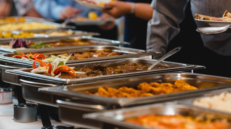 Buffet food service at event banquet, stainless steel catering trays with assorted hot dishes, people serving themselves
