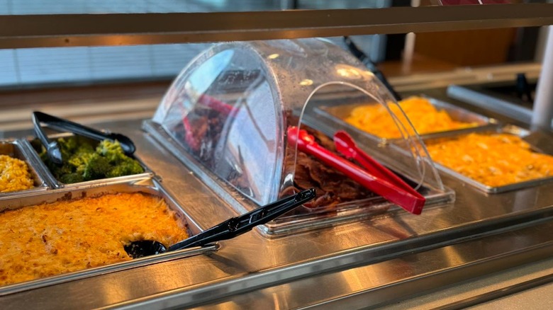 Buffet line showing trays of broccoli, bacon strips, corn and more at Q. Cumbers