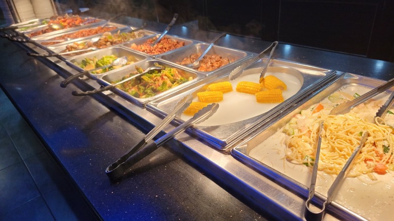 Corn on the cob and various vegetables and dishes on buffet with serving tongs at Hibachi Grill & Supreme Buffet