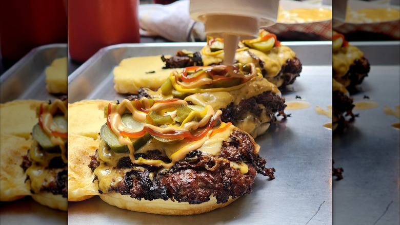 Assembling Gotham Smash Burgers with lots of sauce and pickles at Gotham Burger Social Club in NYC