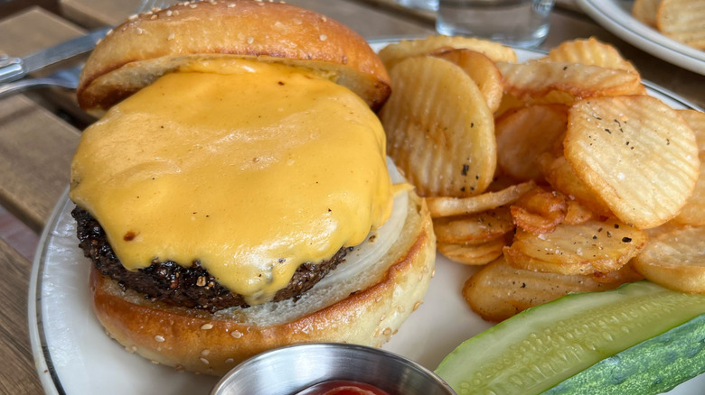 A cheeseburger on a plate with hand cut fries and a pickle