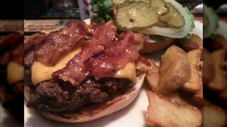 Butch Burger with top bun pulled off showing patty, cheese, and bacon, pickles