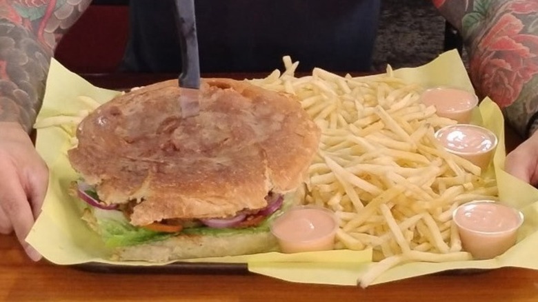Hemi Challenge burger on a tray lined with paper, a pile of french fries and containers of sauce