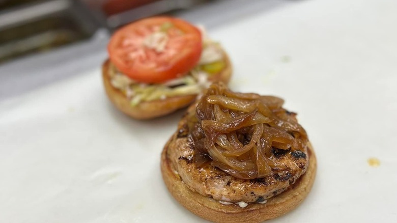 Open turkey burger on paper, patty and grilled onions on bottom bun, lettuce and tomato on top