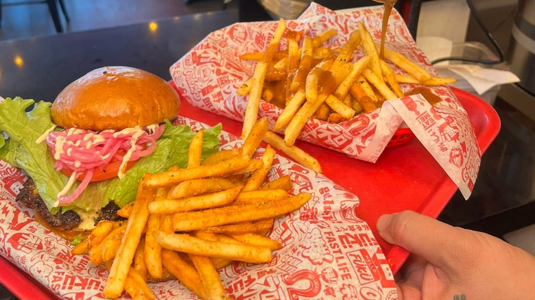 Fukuburger on a paper-lined basket next to side of fries on a tray with another basket of fries