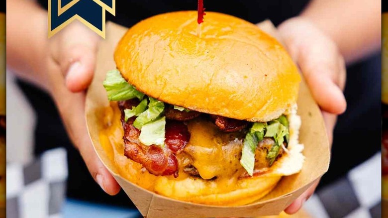 Hands holding a Bobo Burger over a basket of fries with Best Burger Ribbon and text with Al's logo