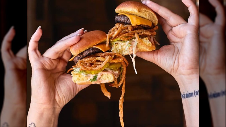 Two hands holding up two Crunch Burger sliders