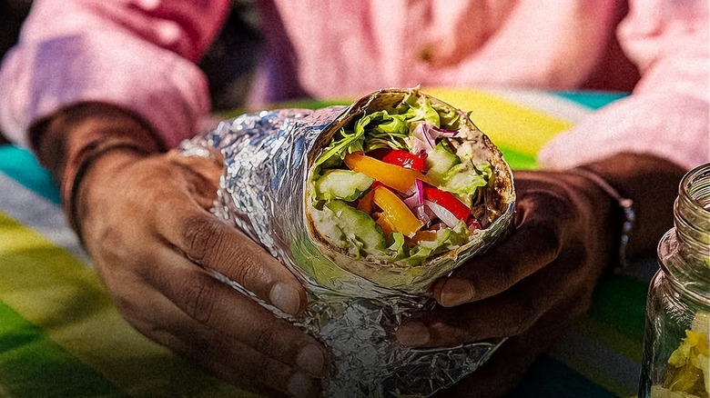 Hands holding a burrito in foil from Cilantro Mexican Grill