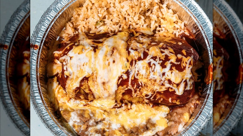 A Gardens of Taxco wet burrito with melted cheese and rice in a to-go container