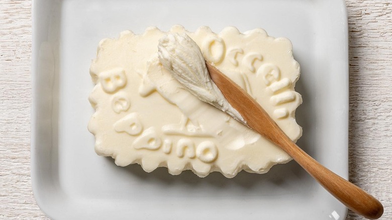 an embossed pat of beppino butter on a white platter with a wooden butter spoon scraping off the top