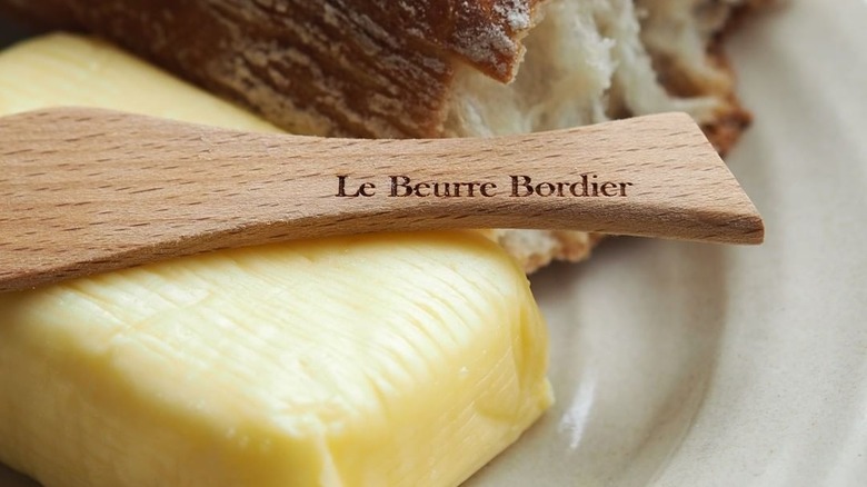 a wooden spoon engraved with le beurre bordier on a pat of butter with a torn of baguette in the background