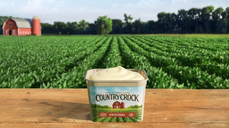 a tub of country crock butter on a wooden bench. fields of green behind with a red barn in the distance