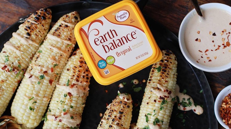 a tub of earth balance on a platter of corn ears and small bowls of mayonnaise and chilli flakes at the side