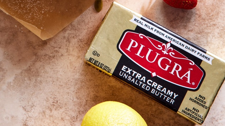 a block of plugra on a marble table with parts of parchment paper and lemon visible