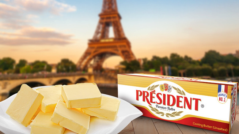 cubes of butter on a white plate in front of a block of president butter. Eiffel tower blurred in the background