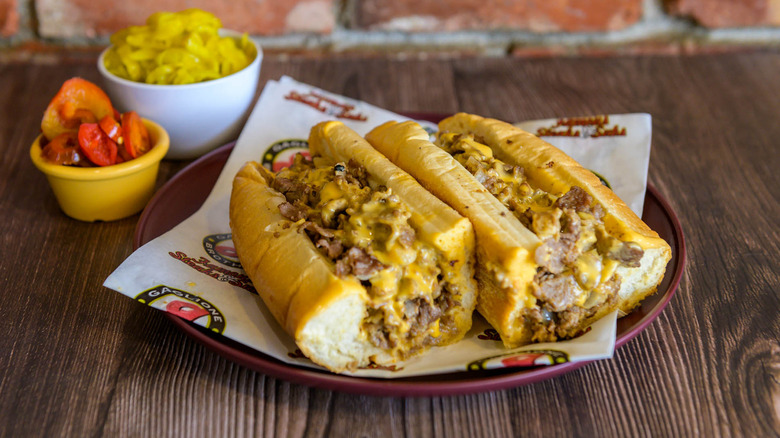 A Gaglione Brothers cheesesteak cut in half with side of peppers.
